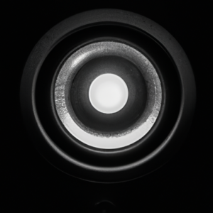 A black and white image of a speaker with a small light glowing at the center.